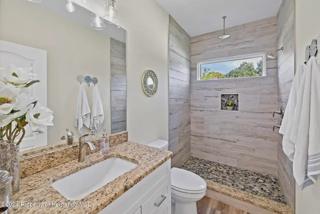 a bathroom with a granite countertop sink a toilet a mirror and shower