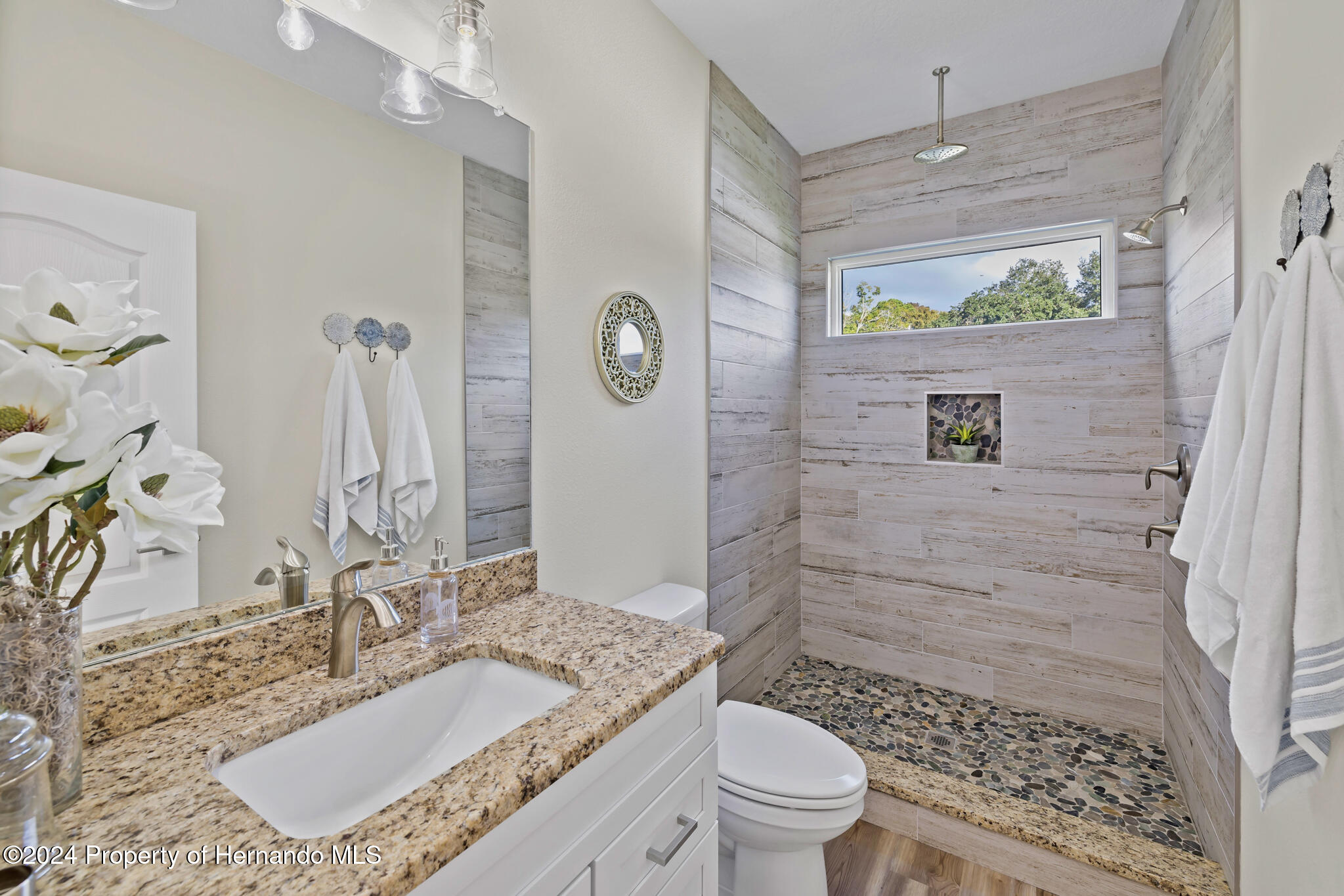 6435 Finance Avenue Weeki Wachee, FL 34607 - Photo 19 of 35 a bathroom with a granite countertop sink a toilet a mirror and shower
