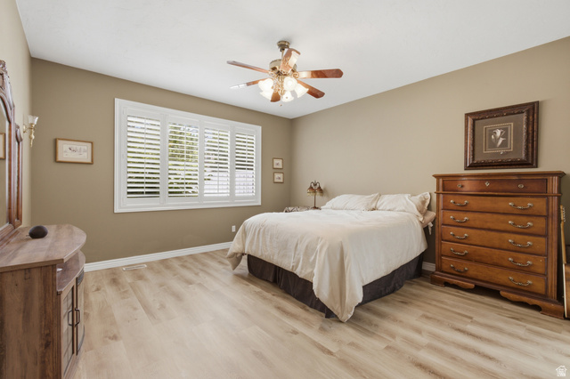 Spacious room featuring light wood-finish flooring, a multi-pane window with white plantation shutters, and a ceiling fan with integrated lighting