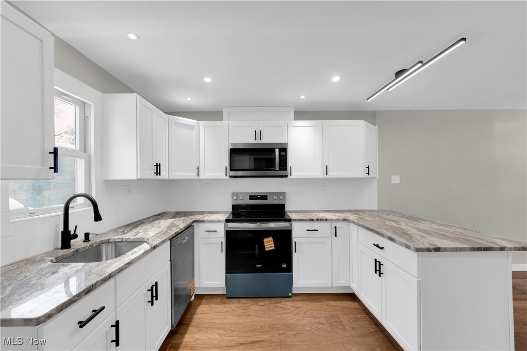 797 Babbitt Road, Unit 15 Euclid, OH 44123 - Photo 6 of 22 Kitchen with stainless steel appliances, light stone counters, light wood finished floors, a peninsula, and white cabinetry