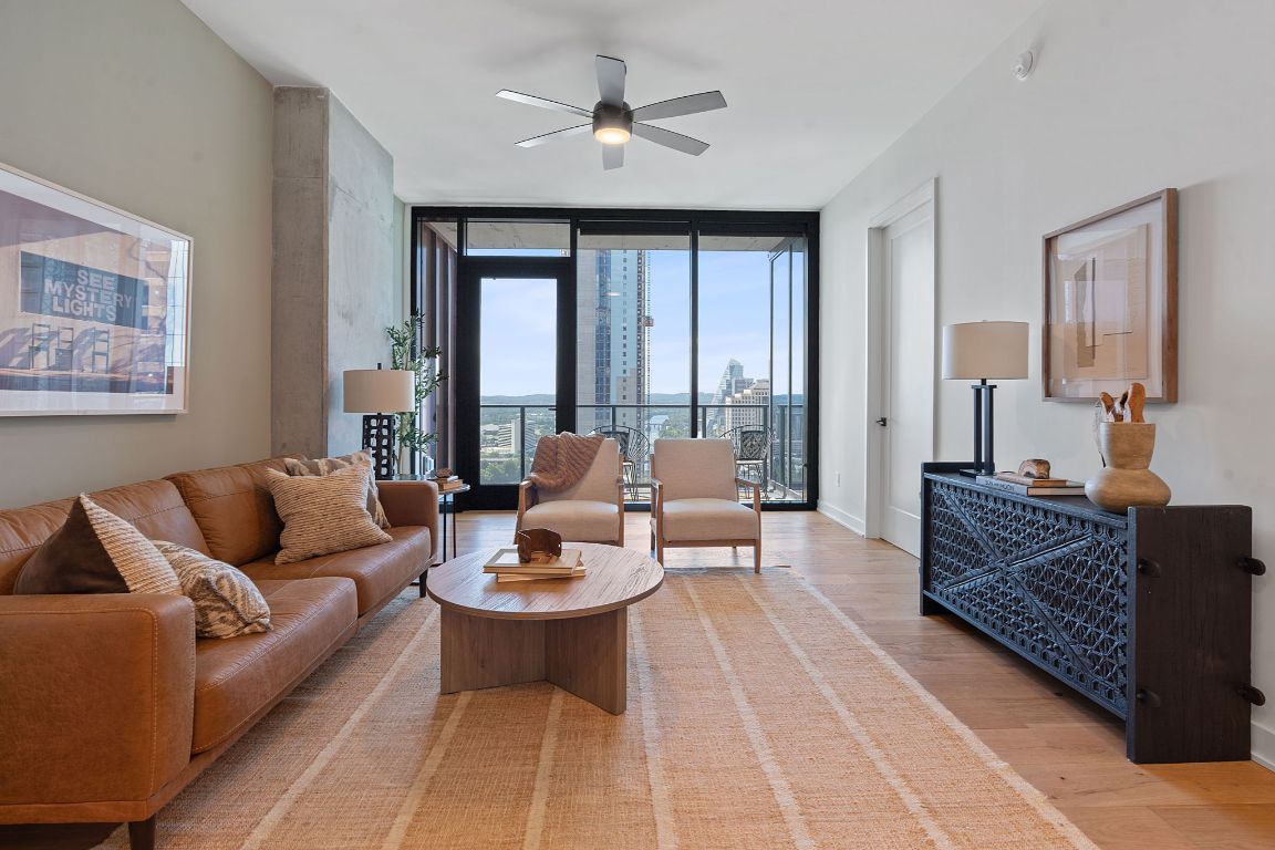 84 East Avenue, Unit 2410 Austin, TX 78701 - Photo 3 of 40 Representative of Property. Living room featuring expansive windows, light wood-style flooring, a view of city, and ceiling fan