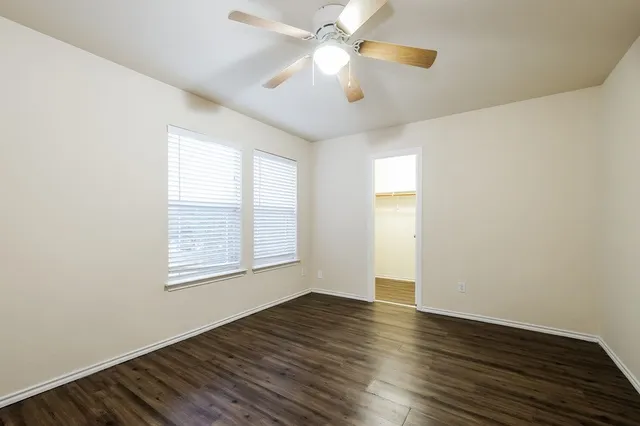 an empty room with wooden floor chandelier fan and windows