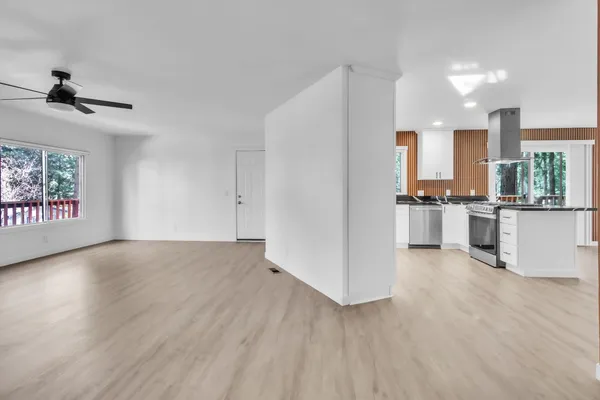 an empty room with wooden floor kitchen view and windows