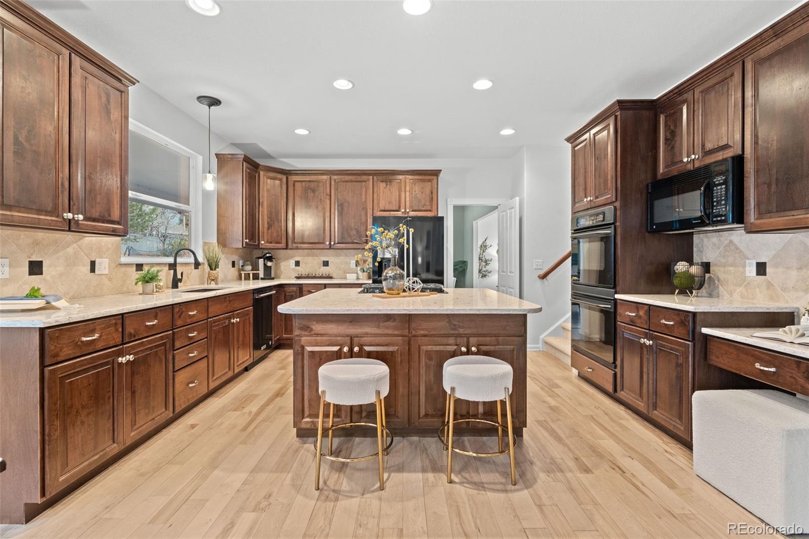 10683 Amesbury Way Highlands Ranch, CO 80126 - Photo 12 of 44 a kitchen with stainless steel appliances granite countertop wooden cabinets stools a stove a sink and a refrigerator