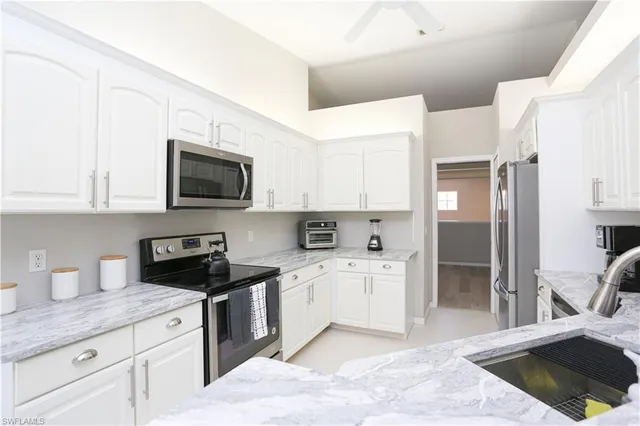 a kitchen with stainless steel appliances kitchen island granite countertop a refrigerator sink and white cabinets