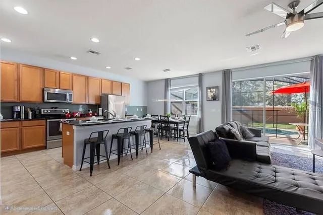 a living room with stainless steel appliances kitchen island granite countertop a stove top oven a sink a dining table and chairs with the view of kitchen