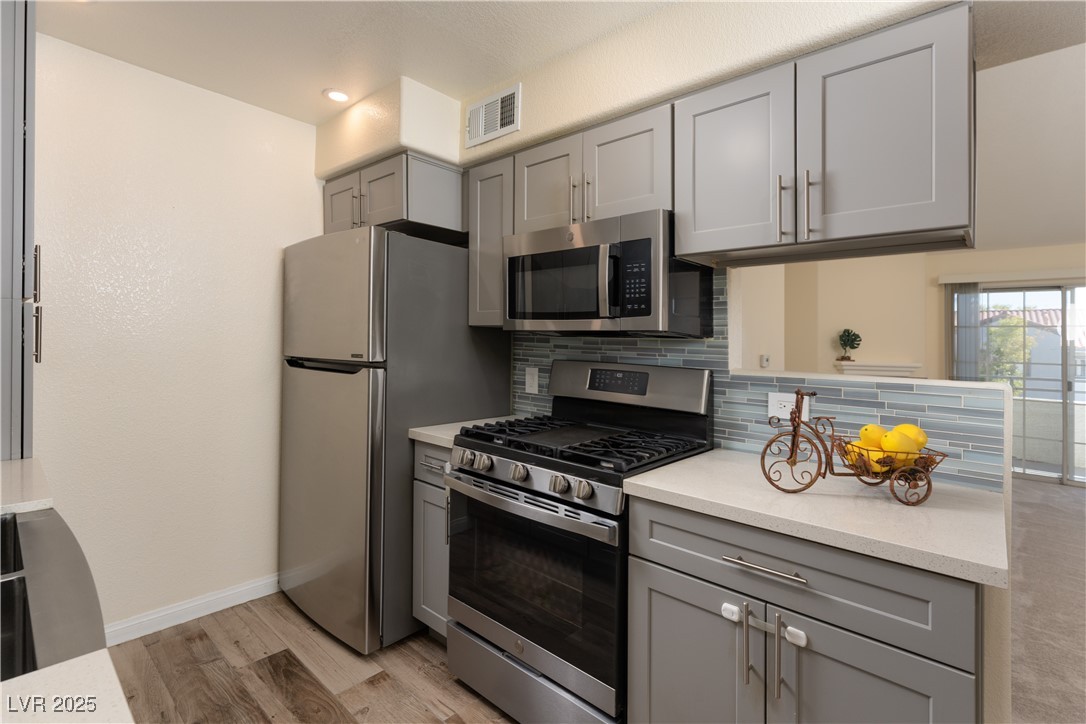 3318 North Decatur Boulevard, Unit 2143 Las Vegas, NV 89130 - Photo 2 of 34 Kitchen with gray cabinetry, appliances with stainless steel finishes, tasteful backsplash, light wood-type flooring, and light stone countertops