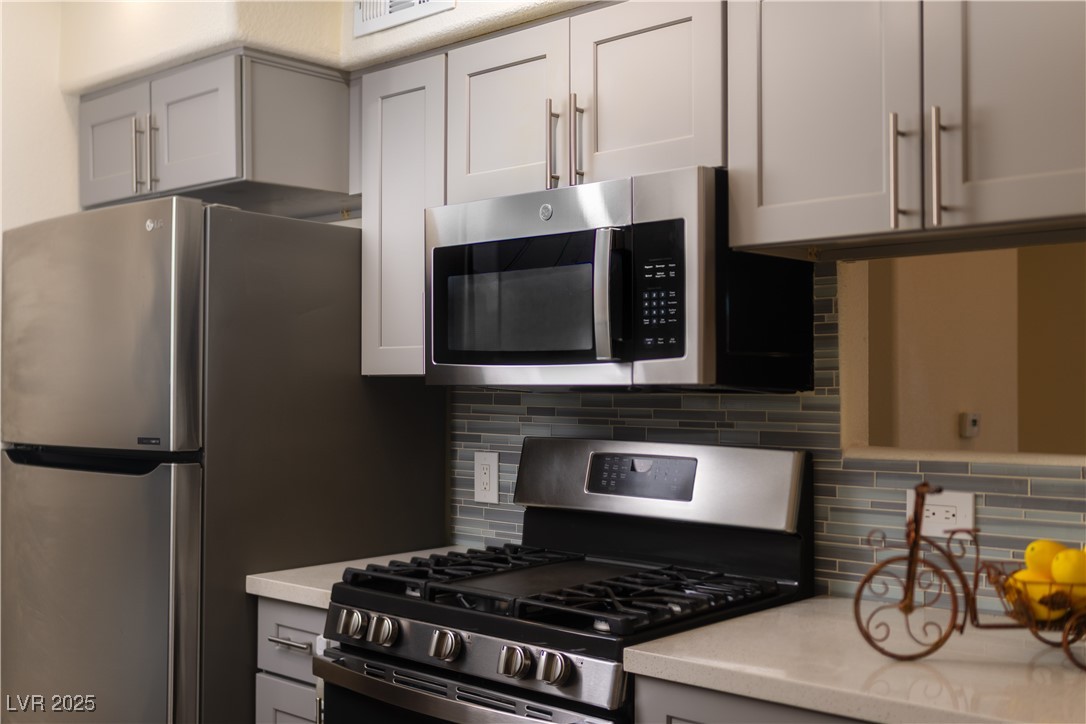 3318 North Decatur Boulevard, Unit 2143 Las Vegas, NV 89130 - Photo 5 of 34 Kitchen with gray cabinets, stainless steel appliances, backsplash, and light stone countertops
