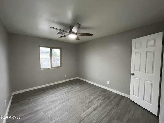 an empty room with wooden floor ceiling fan and windows