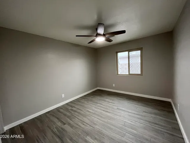 an empty room with wooden floor ceiling fan and windows