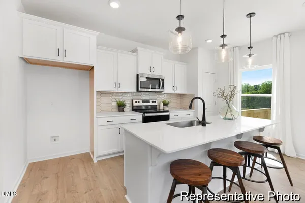 a kitchen with stainless steel appliances granite countertop a stove a sink a microwave a dining table and chairs with white cabinets