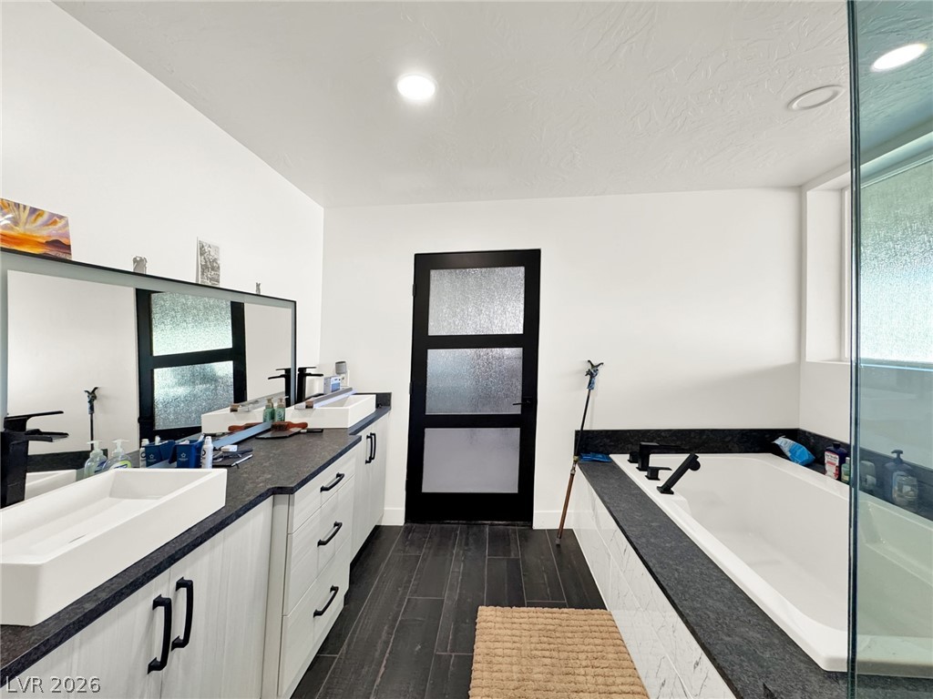 9393 North 93rd Highway Caliente, NV 89008 - Photo 16 of 41 Luxurious primary bathroom featuring a spacious soaking tub, dual vanities, and rich wood-look flooring.