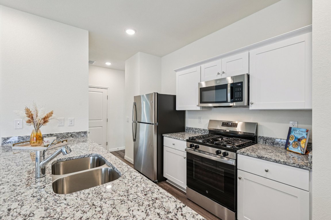 1516 Morris Loop San Marcos, TX 78666 - Photo 14 of 40 Kitchen featuring appliances with stainless steel finishes, light stone countertops, white cabinets, recessed lighting, and dark wood-type flooring