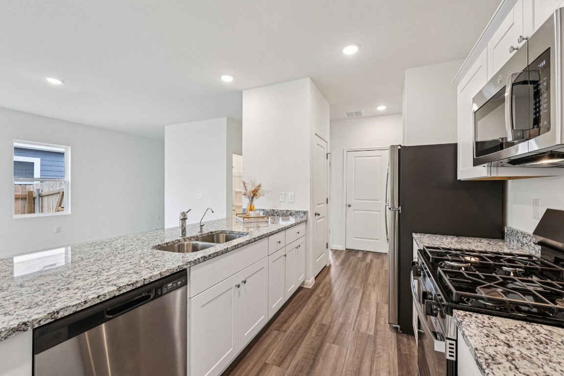 1516 Morris Loop San Marcos, TX 78666 - Photo 15 of 40 Kitchen with appliances with stainless steel finishes, white cabinetry, light stone counters, dark wood-style floors, and recessed lighting