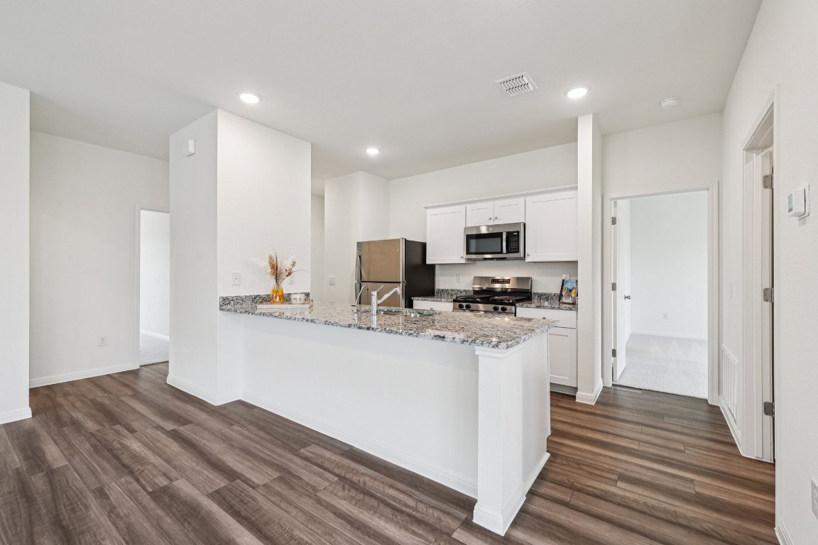 1516 Morris Loop San Marcos, TX 78666 - Photo 16 of 40 Kitchen with white cabinetry, a peninsula, stainless steel appliances, light stone counters, and dark wood-style flooring