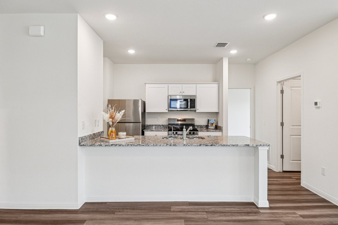 1516 Morris Loop San Marcos, TX 78666 - Photo 5 of 40 Kitchen featuring white cabinets, stainless steel appliances, light stone countertops, a peninsula, and dark wood-style flooring
