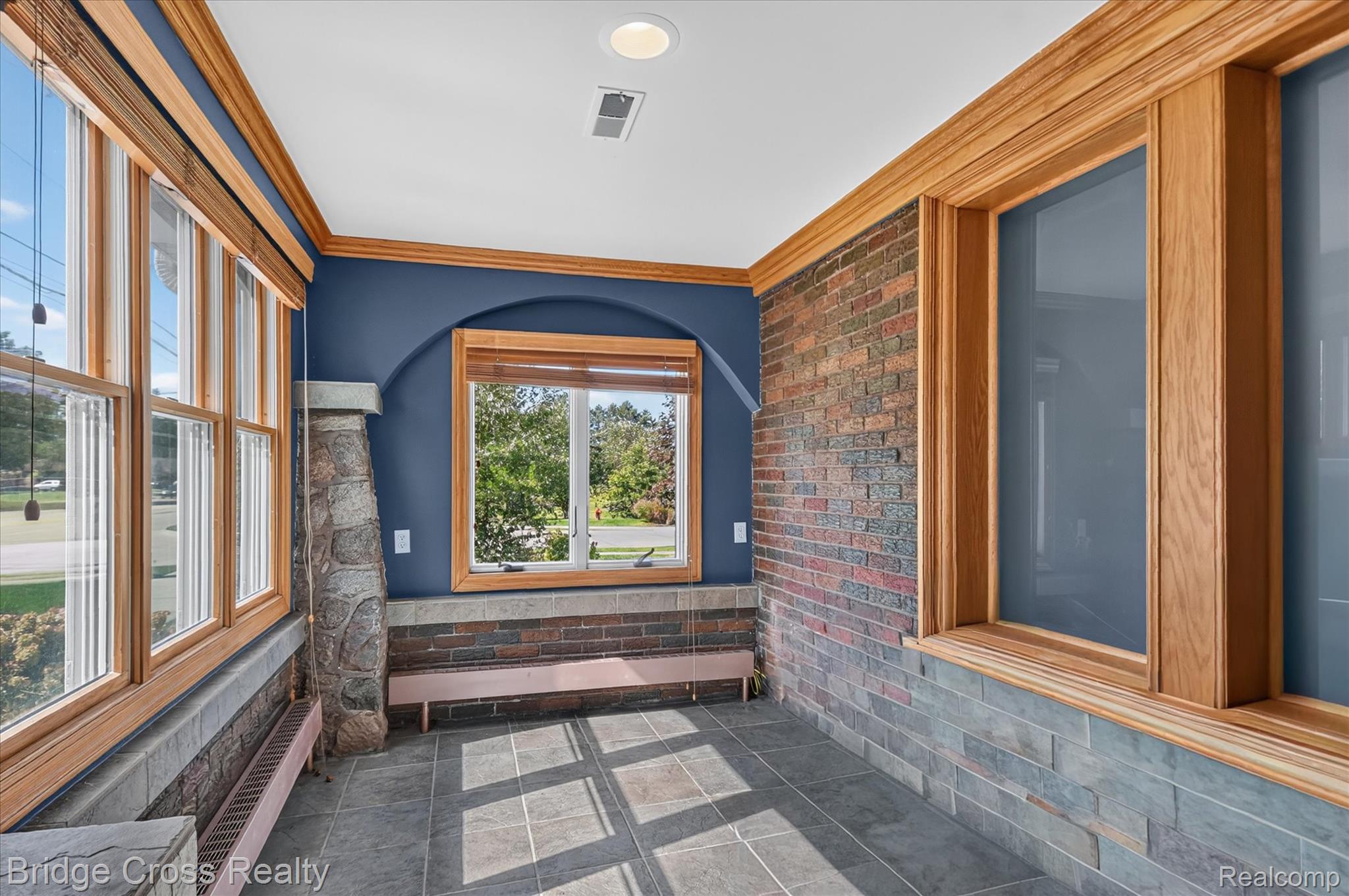 285 East Long Lake Road Troy, MI 48085 - Photo 7 of 49 Sunroom featuring expansive wood-trimmed windows, exposed brick walls, slate-finish tile flooring in geometric patterns, blue accent walls, and a central brick fireplace with wood mantel and seating bench