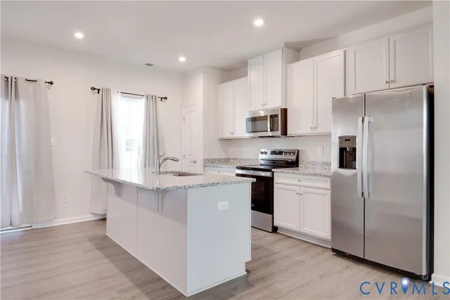 a kitchen with stainless steel appliances granite countertop a refrigerator a stove a sink and white cabinets with wooden floor