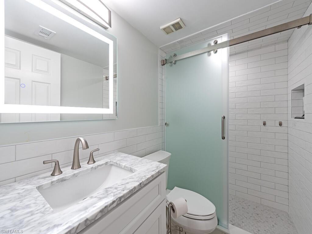 4556 Andover Way, Unit E104 Naples, FL 34112 - Photo 10 of 12 a bathroom with a granite countertop sink toilet a mirror and shower