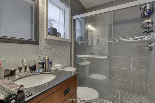 a bathroom with a granite countertop sink a toilet a mirror and shower