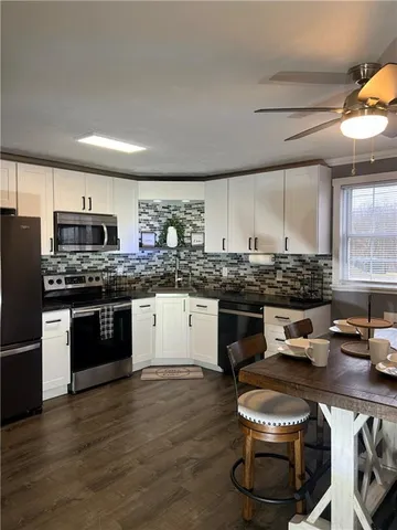 a kitchen with stainless steel appliances a stove a sink dishwasher a refrigerator and white cabinets with wooden floor