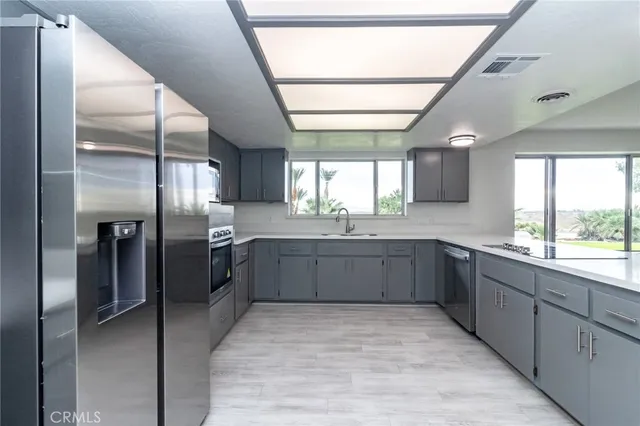 a large kitchen with stainless steel appliances kitchen island granite countertop a refrigerator a sink dishwasher a stove and white countertops with wooden floor