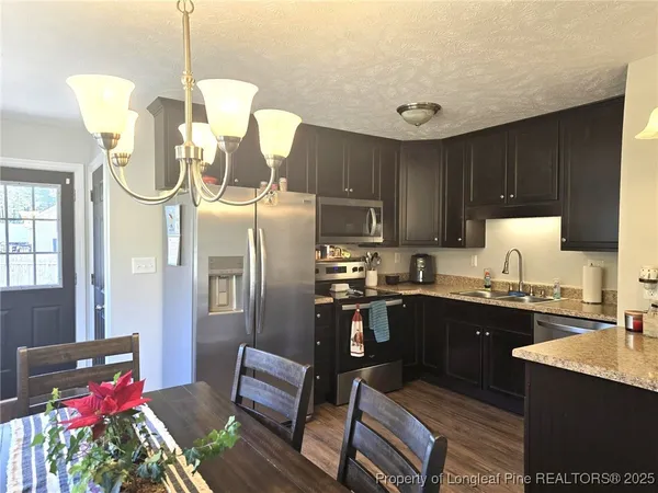 a kitchen with stainless steel appliances granite countertop a refrigerator a sink dishwasher a dining table and chairs with wooden floor