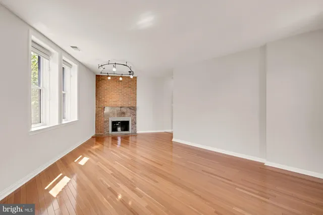 a view of an empty room with wooden floor fireplace and a window