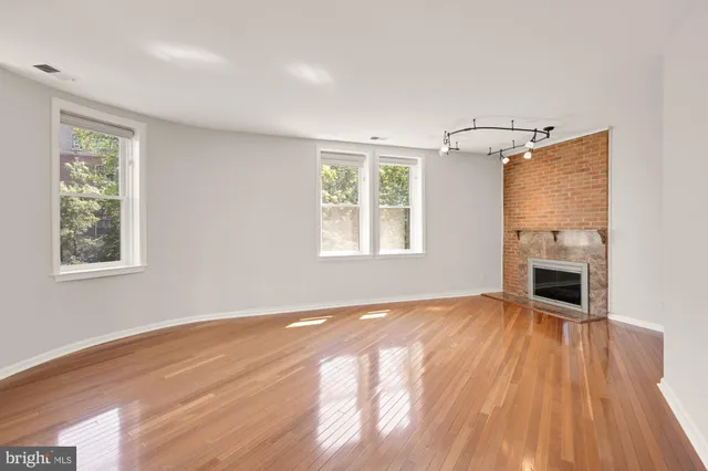 a view of an empty room with wooden floor fireplace and a window
