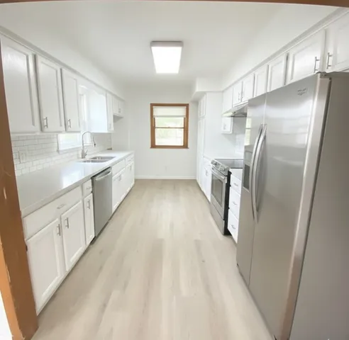 a kitchen with stainless steel appliances granite countertop a refrigerator a sink dishwasher a stove and white countertops with wooden floor