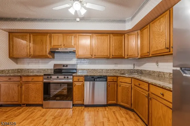 a kitchen with stainless steel appliances granite countertop wooden cabinets a stove a sink and dishwasher with wooden floor