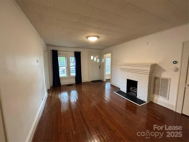a view of an empty room with wooden floor fireplace and a window