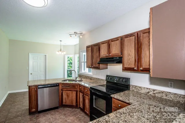 a kitchen with granite countertop a stove top oven a sink a counter space and cabinets