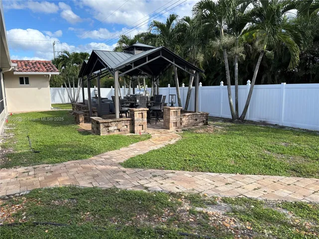 a view of a patio with a table and chairs under an umbrella with a barbeque grill and plants
