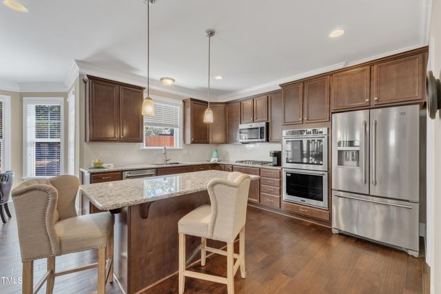 a kitchen with stainless steel appliances granite countertop a refrigerator a stove a sink a dining table and chairs with wooden floor