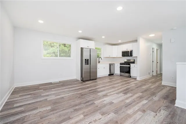 an empty room with stainless steel appliances wooden floor and windows