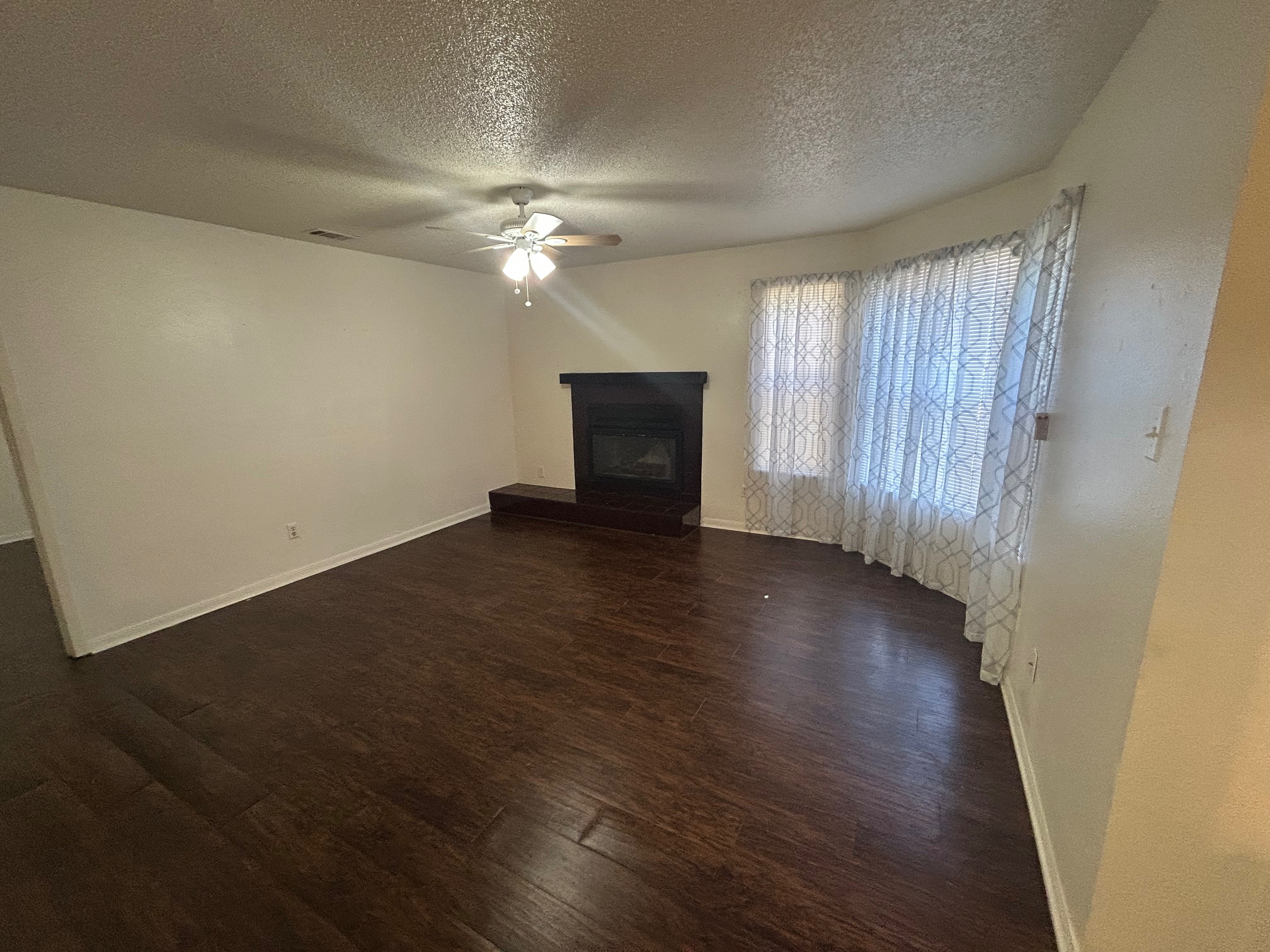 8812 Schick Road, Unit C Austin, TX 78729 - Photo 6 of 12 Unfurnished living room featuring a textured ceiling, dark wood-style floors, a glass covered fireplace, and a ceiling fan