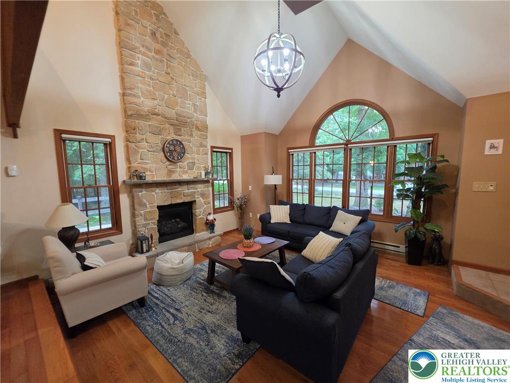 211 Murphy Circle Bushkill, PA 18324 - Photo 4 of 28 A striking stone fireplace anchors this living space, featuring towering vaulted ceilings and natural wood flooring.