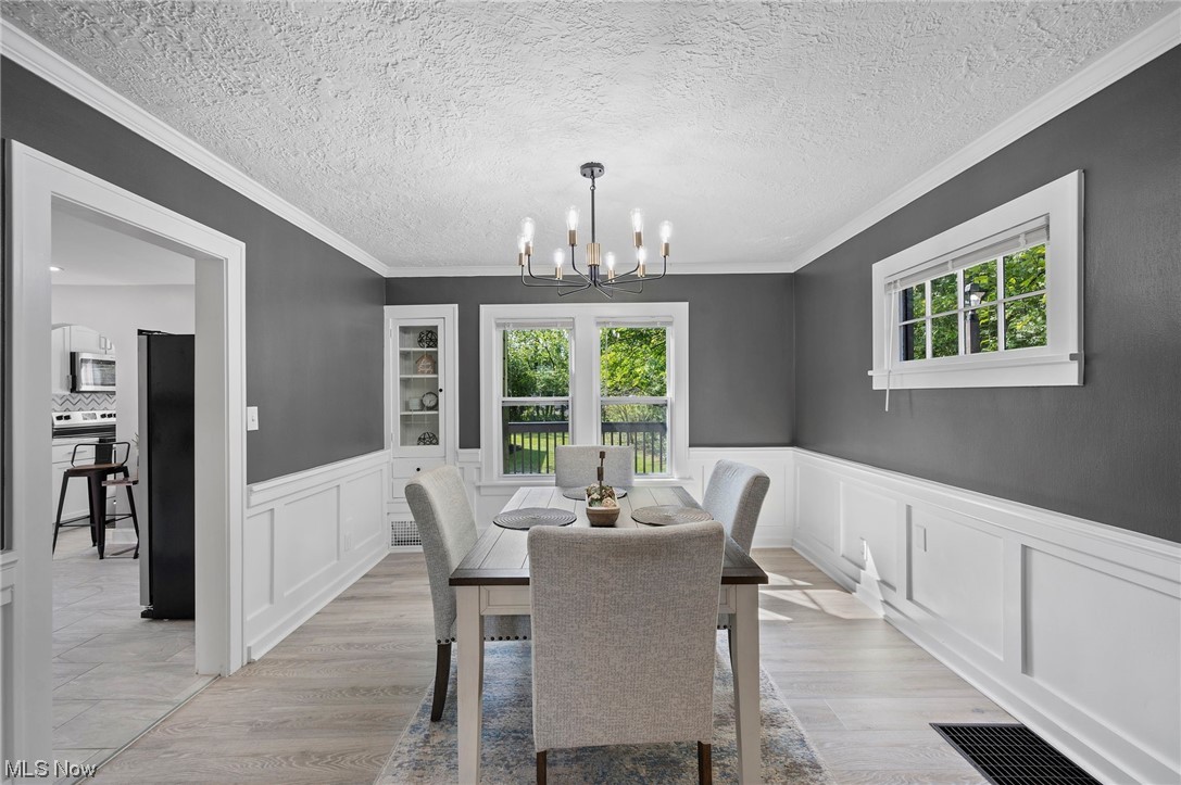 1022 Englewood Road Cleveland, OH 44121 - Photo 19 of 33 Dining space featuring a chandelier, light wood-type flooring, ornamental molding, and a textured ceiling