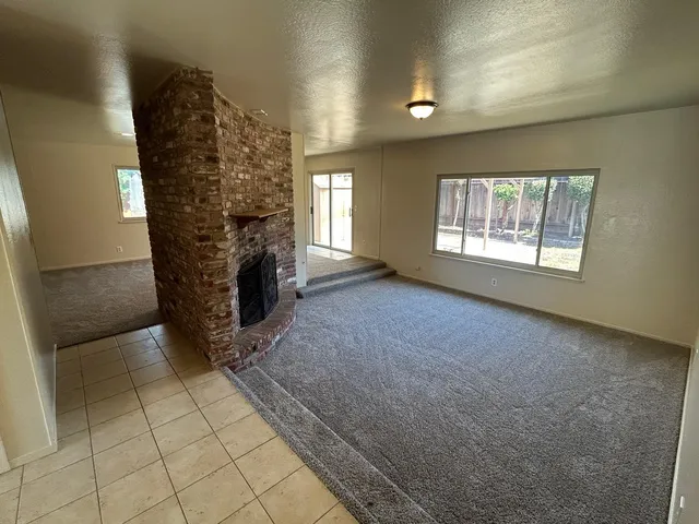 an empty room with wooden floor fireplace and windows