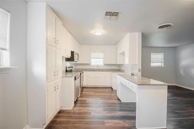 a large white kitchen with granite countertop a sink and dishwasher a refrigerator with wooden floors