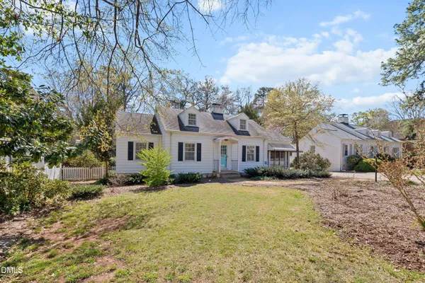 a view of a white house next to a yard with plants and large trees