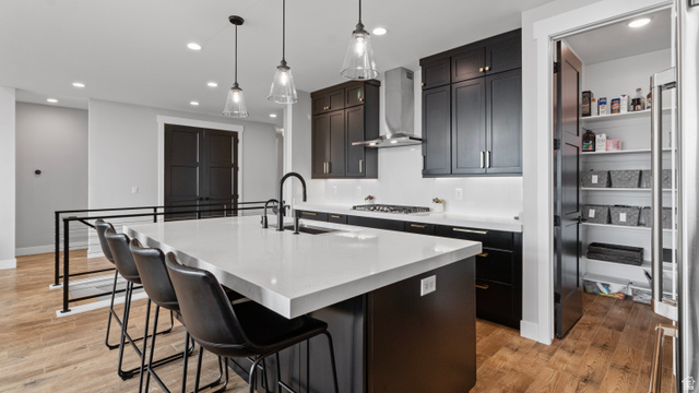 355 East Overlook Loop Hideout, UT 84036 - Photo 11 of 40 Modern kitchen featuring a large island with seating, a built-in sink with a matte black faucet, pendant lighting, dark cabinetry, and wood-finish flooring