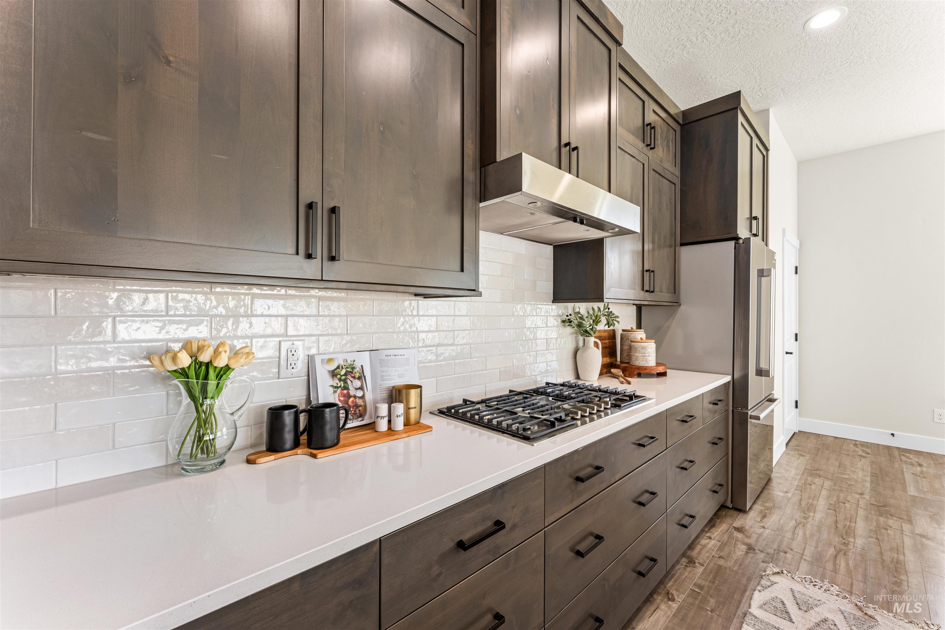 2787 West Warlander Street Meridian, ID 83642 - Photo 11 of 34 Kitchen featuring a textured ceiling, dark wood finish cabinetry, light wood finished floors, stainless steel appliances, and backsplash