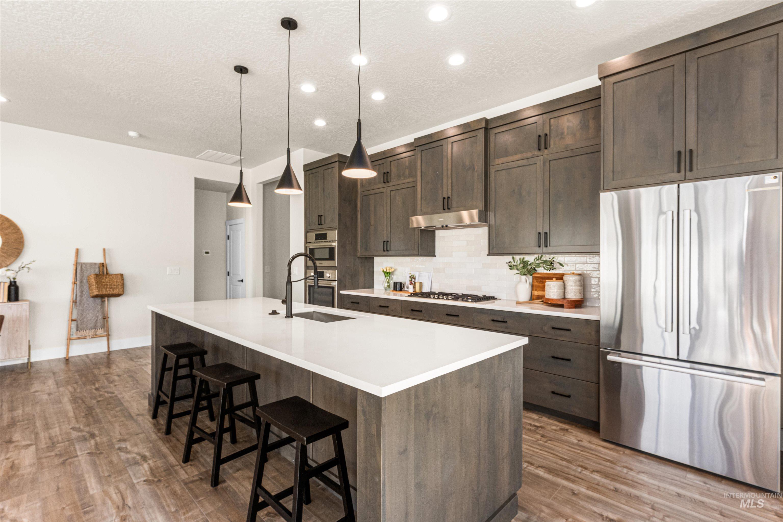 2787 West Warlander Street Meridian, ID 83642 - Photo 12 of 34 Kitchen with stainless steel appliances, a kitchen breakfast bar, decorative backsplash, hanging light fixtures, and a textured ceiling