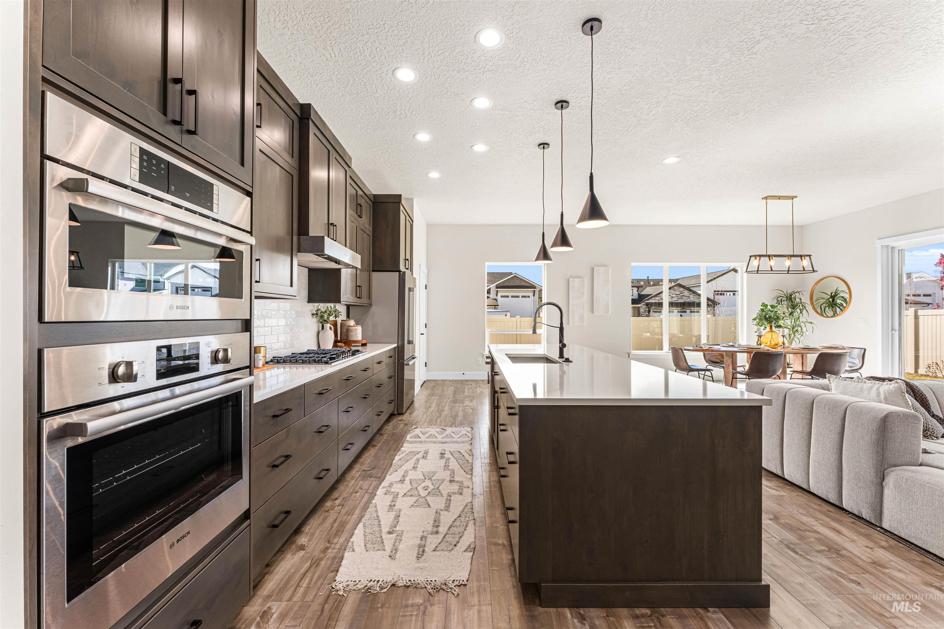 2787 West Warlander Street Meridian, ID 83642 - Photo 32 of 34 Kitchen featuring dark wood finish cabinetry, stainless steel appliances, open floor plan, an island with sink, and light wood-style floors