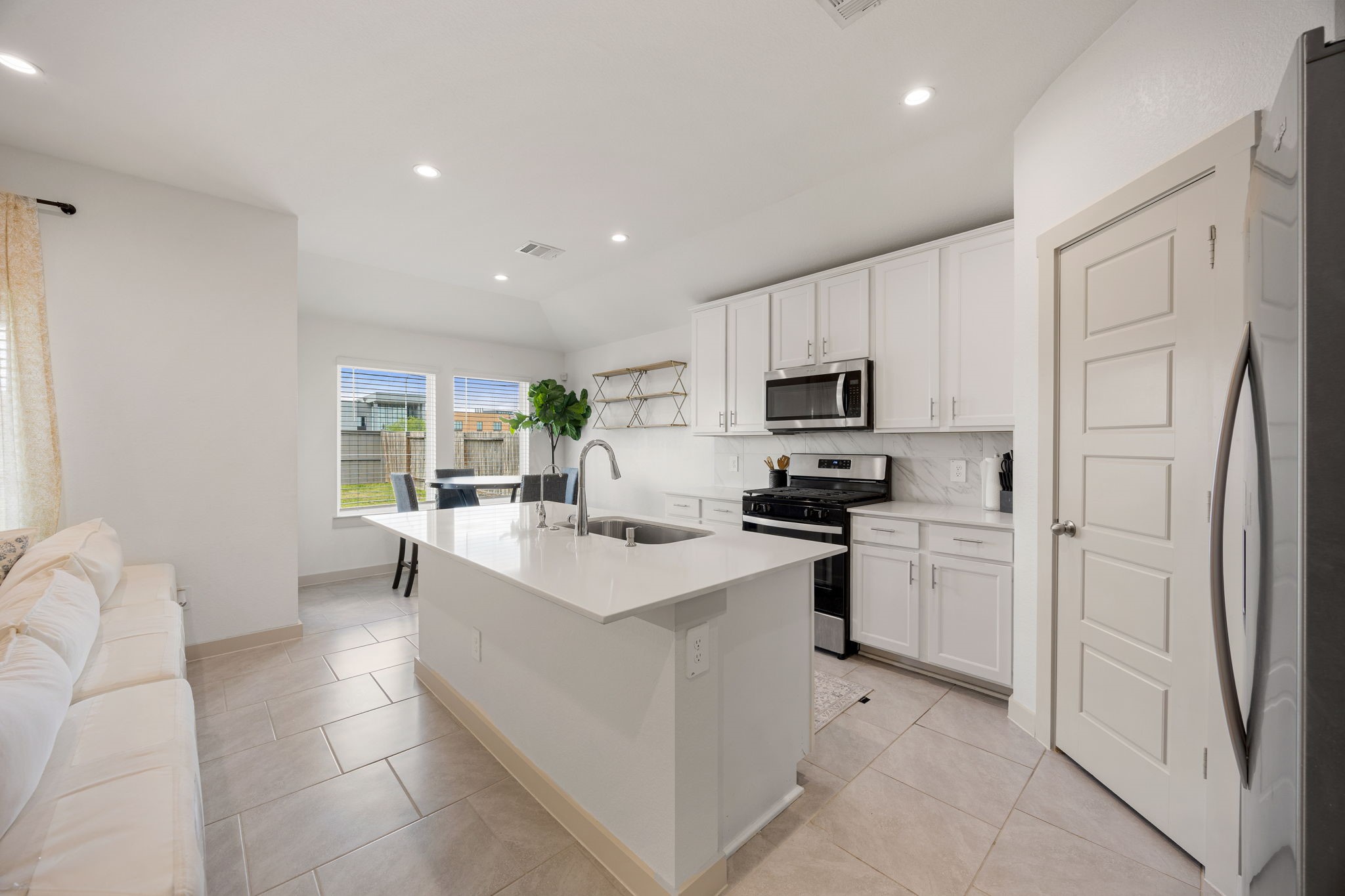 711 Alpine Fls Road Rosharon, TX 77583 - Photo 5 of 20 The seamless transition into the gourmet kitchen features crisp white cabinetry, elegant quartz countertops, and a massive central island with a built-in breakfast bar. Recessed lighting and a contemporary ceiling fan complete this expansive, cohesive space, offering a clean canvas for your personal style.