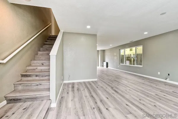 a view of an empty room with wooden floor and fan