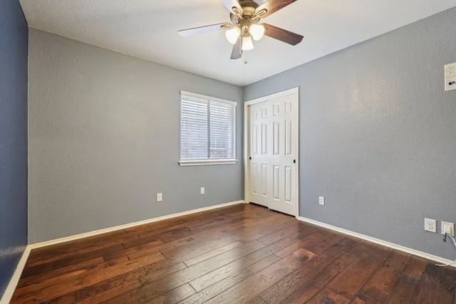 an empty room with wooden floor chandelier fan and windows