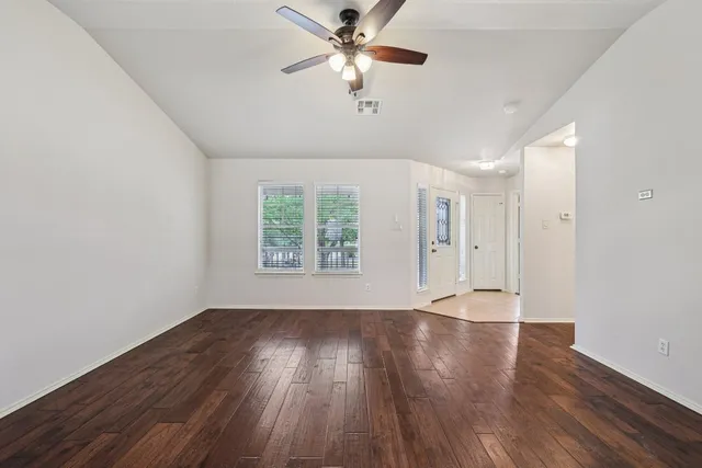 an empty room with wooden floor chandelier fan and windows